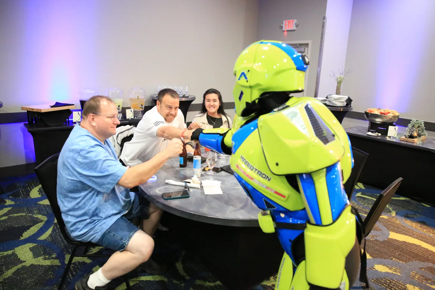 Guests at a table fist-bumping a costumed robot character at The Big Show Wrap-Up